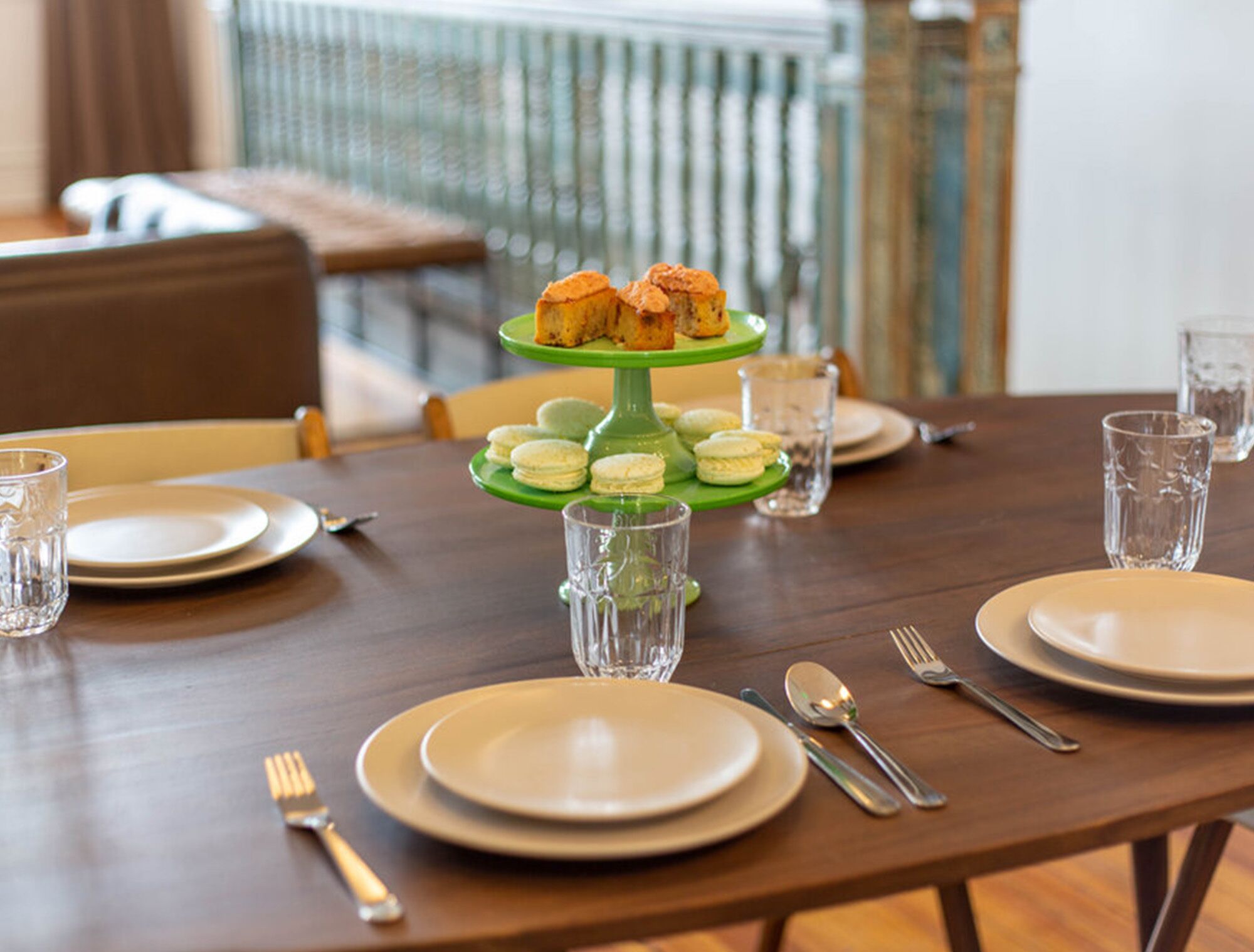 A dining table set with plates, cutlery, glasses, and a green tiered stand holding pastries and macarons.