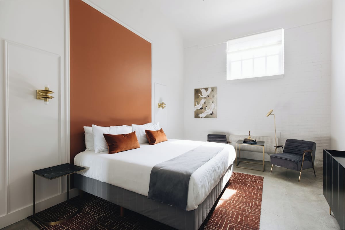 A modern hotel room with a large bed, a desk, a chair, and a view of the city.