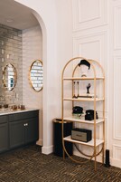 Un baño moderno con tocador, estante dorado con adornos y piso estampado.
