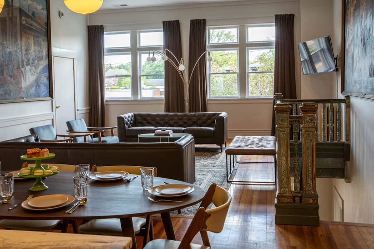 A dining area with a round table set for four, a sofa, and a staircase with ornate railings.