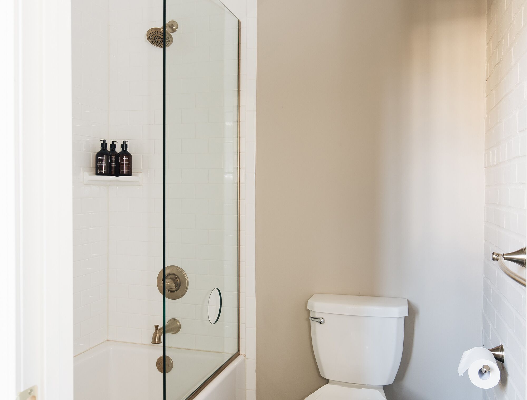 A bathroom with a glass-enclosed shower, a toilet, and a shelf with toiletries.