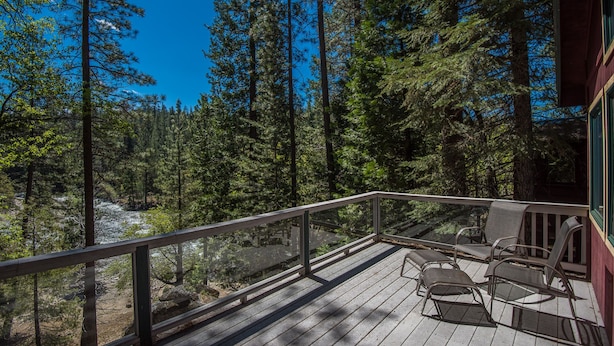 A wooden deck with metal chairs and a glass railing overlooking a forest. - Yosemite Riverside Retreat - Gorgeous Views! Wood burning Stove! (Wawona)