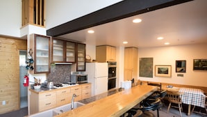 A modern kitchen with a wooden bar area, stainless steel appliances, and a dining table with chairs. - Yosemite Riverside Retreat - Gorgeous Views! Wood burning Stove! (Wawona)