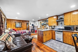 Een gezellige woonkamer met een leren bank en een open haard, een keuken met houten kastjes en moderne apparatuur, en een eethoek met een tafel en stoelen.