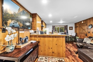 Een rustiek houten interieur met een bar, een naaimachine en een groot raam met uitzicht op een bergachtig landschap.