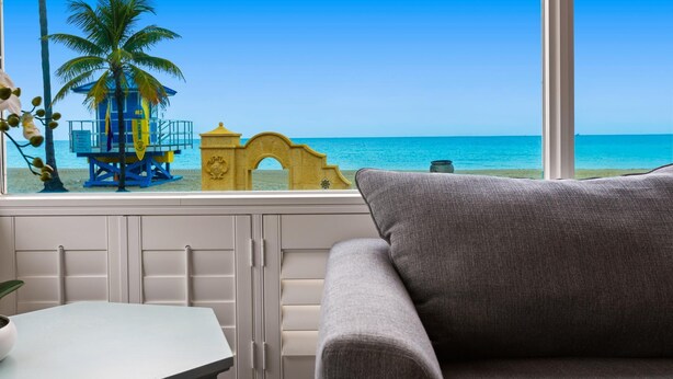 Una habitación con vista a una playa, una torre de salvavidas y un arco amarillo.