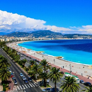 Un paysage urbain côtier avec une large route, des palmiers et une plage bordée d’une eau bleu clair.
