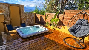 Une terrasse en bois avec un jacuzzi, une chaise berçante et un mur en pierre.