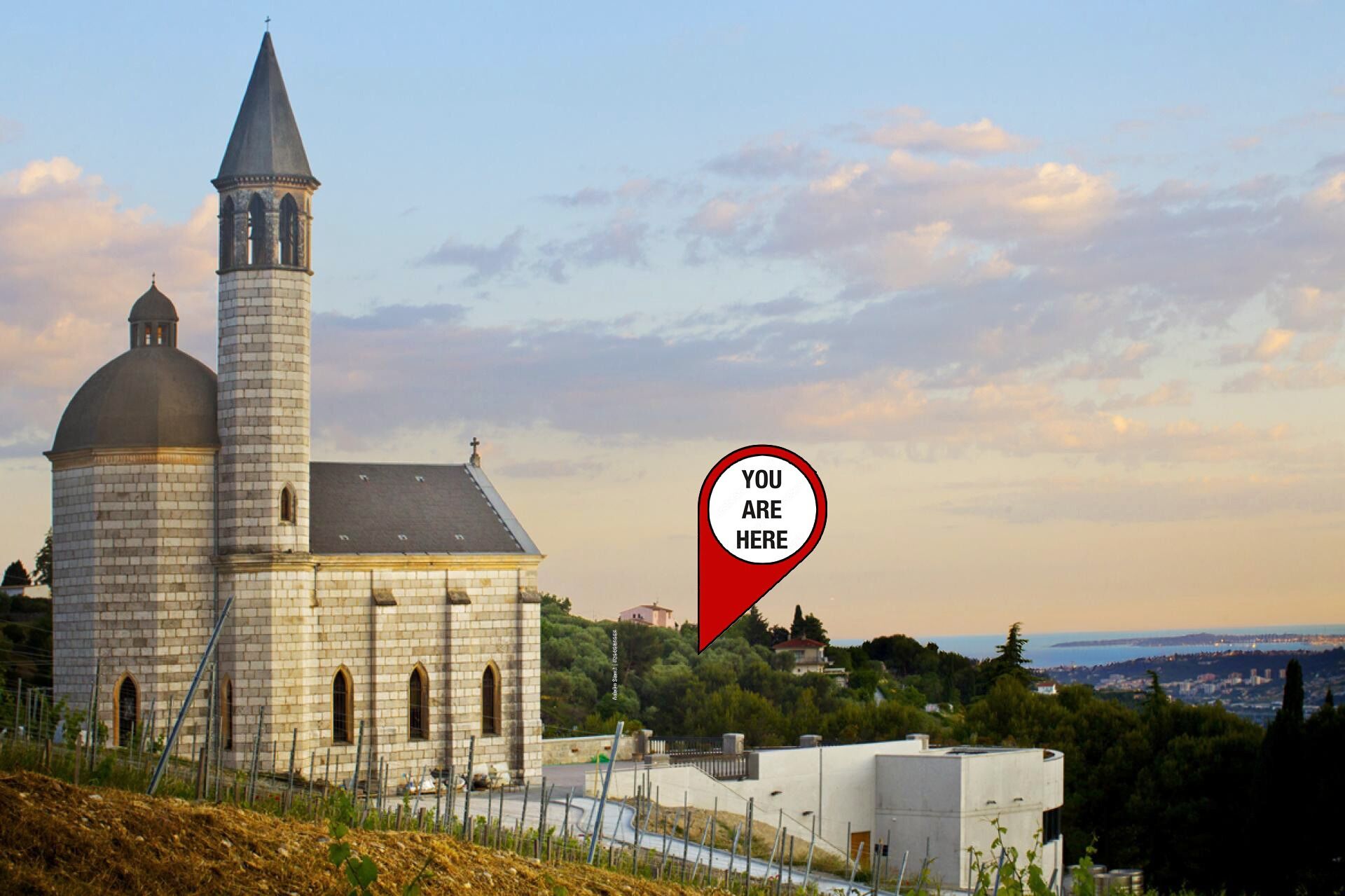 Une église dotée d’un haut clocher et d’un dôme, entourée de verdure et offrant une vue sur une ville au loin.