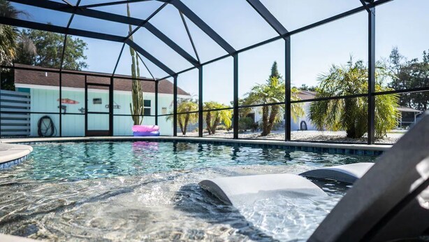 A swimming pool with a hot tub area, surrounded by a glass enclosure, and palm trees in the background. - The Pelican (Nokomis)