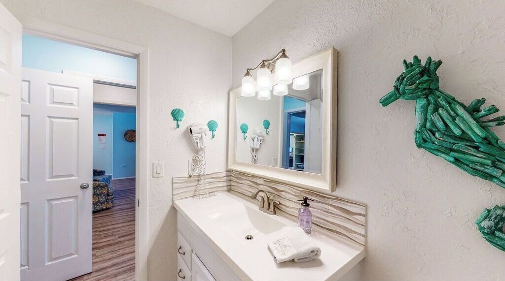 A bathroom with a white sink, a mirror, and a green wall decoration.