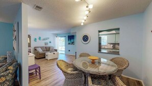 A living room with a round wicker table and chairs, a sofa, a small purple stool, and a clock on the wall. - The Pelican (Nokomis)
