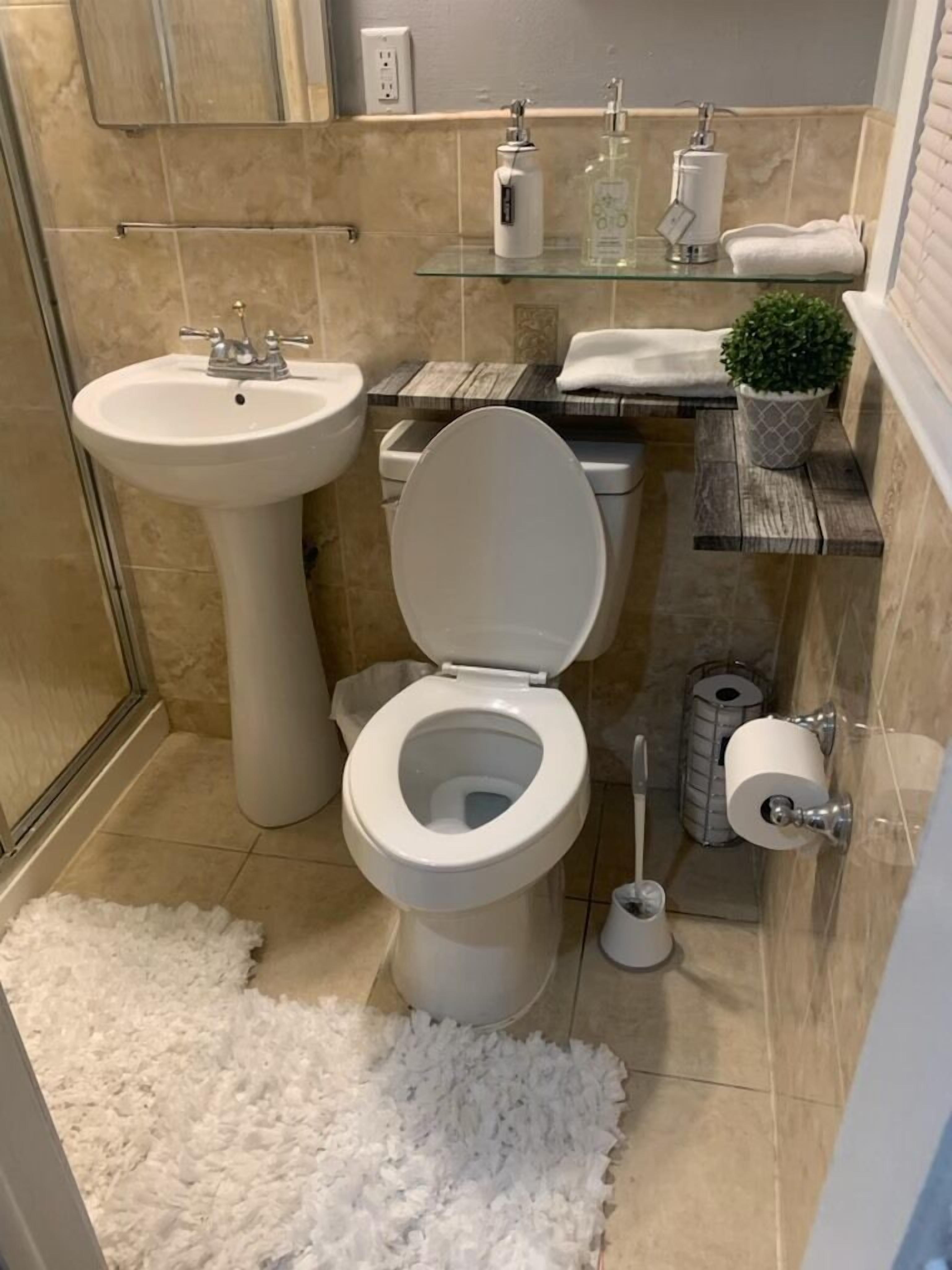 Un baño con lavamanos pedestal, inodoro y repisa de vidrio con artículos de aseo.
