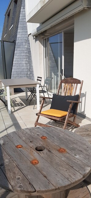 A wooden table and a wooden chair with a cushion on an outdoor patio.