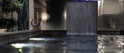 A modern indoor pool area with a water feature, a sculpture, and a wall with abstract art.