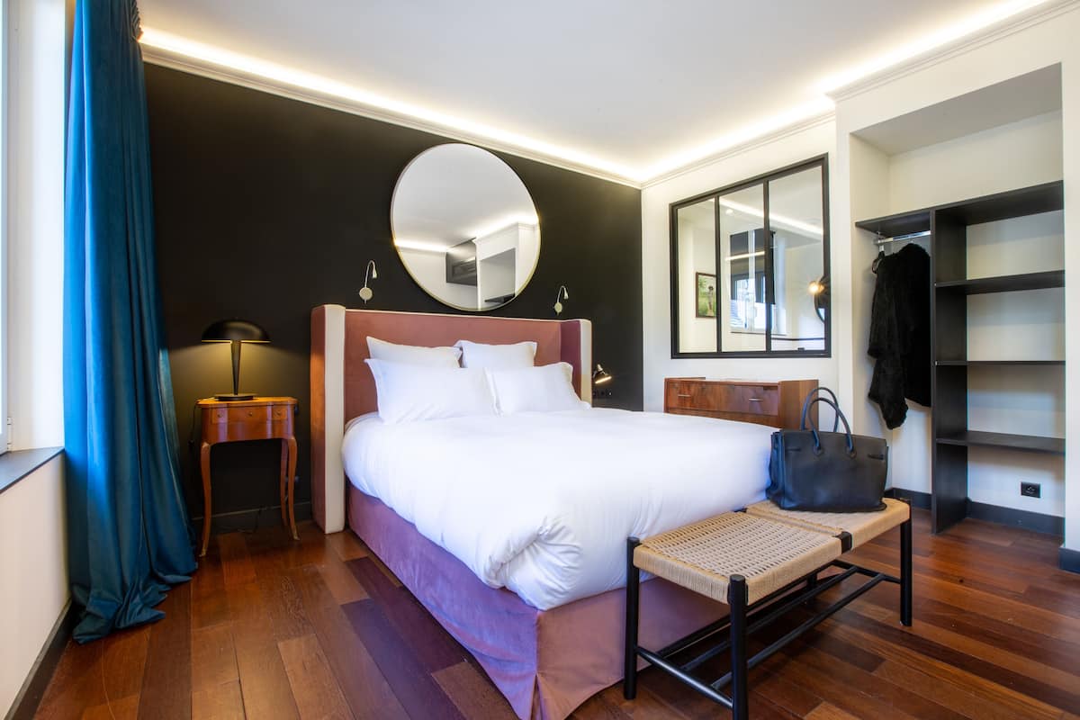 Ein Hotelzimmer mit einem großen Bett, einem Nachttisch, einem Spiegel, einem Kleiderschrank und einer Bank.