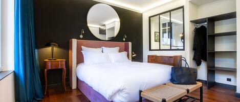 Habitación de hotel con una cama grande, una mesita de noche, un espejo, un armario y un banco.