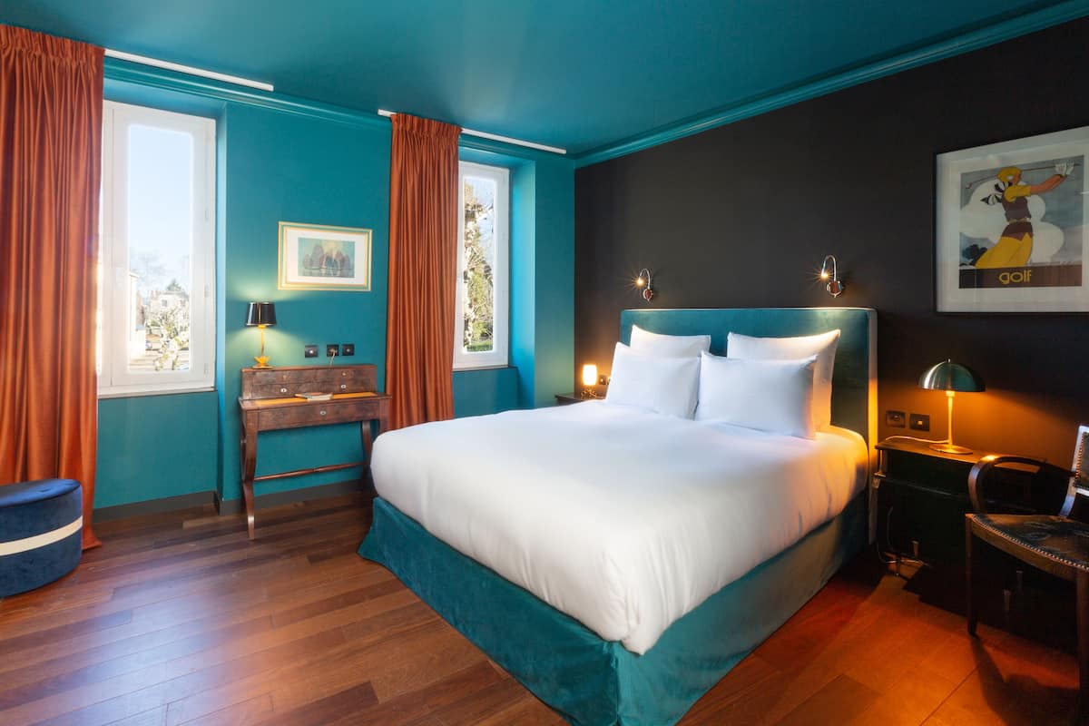 Ein Hotelzimmer mit einem großen Bett, einem Schreibtisch, einem Sessel, einer Lampe und einem Bild an der Wand.