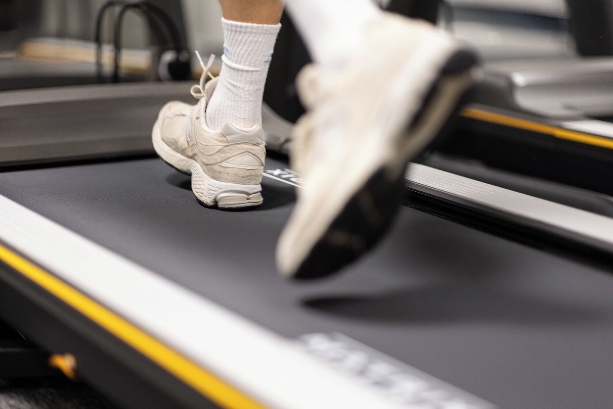 Gros plan sur les pieds d’une personne sur un tapis de course, avec une attention particulière portée aux chaussures de course et à la surface du tapis.