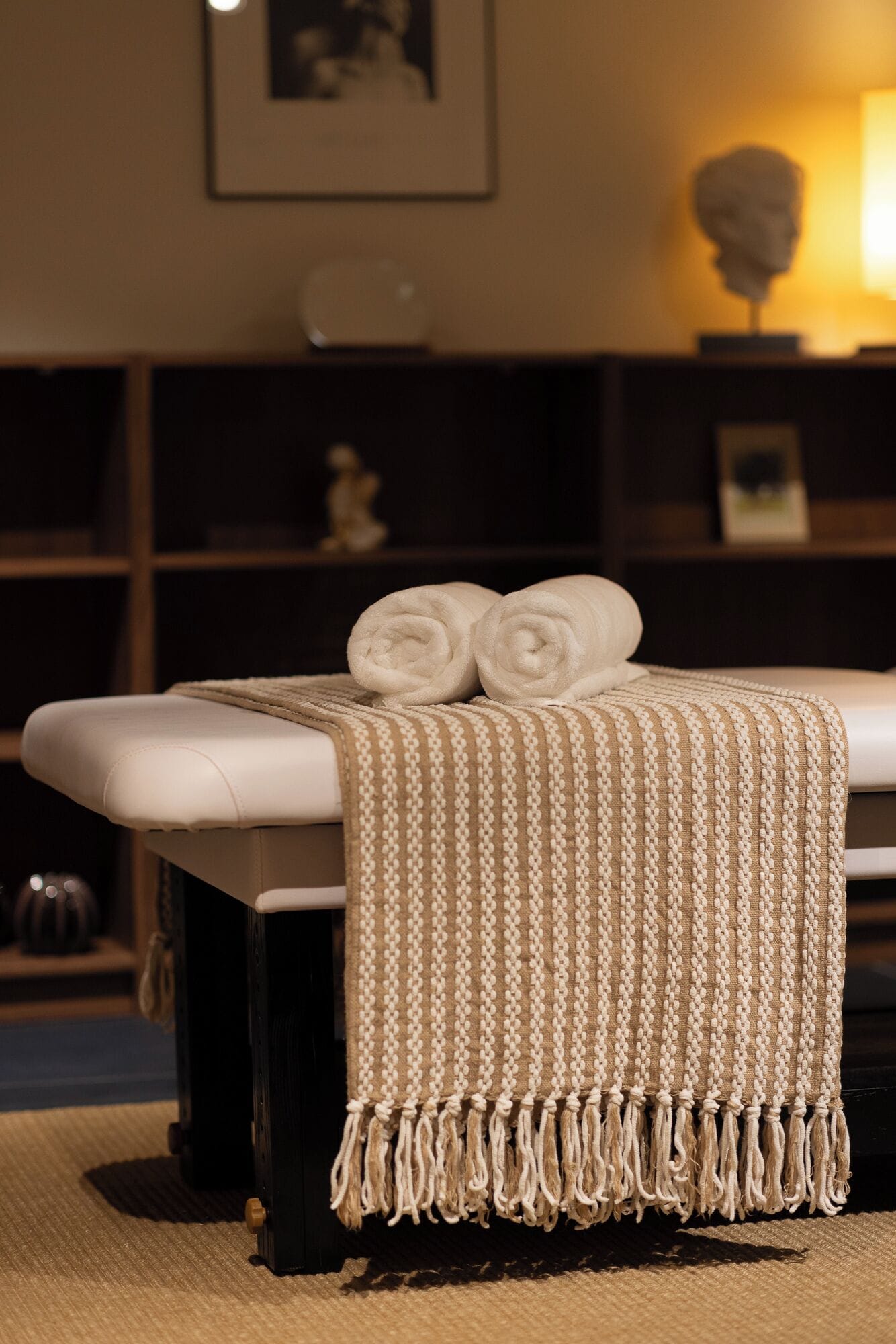 A massage table with a beige towel and a woven blanket.