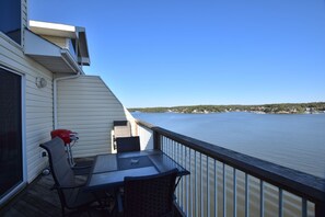 Een balkon met een tafel en stoelen, met uitzicht op een rustig wateroppervlak en een verre kustlijn.