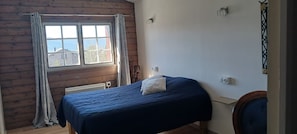 A room with a bed, a window with curtains, a radiator, and a wall-mounted light switch.