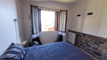 Une chambre avec un lit, une fenêtre avec des rideaux, un radiateur et un mur en pierre.