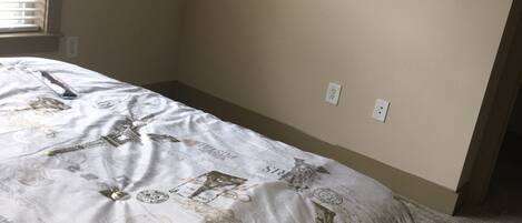 A bedroom with a bed, a mounted TV, and a window with blinds.