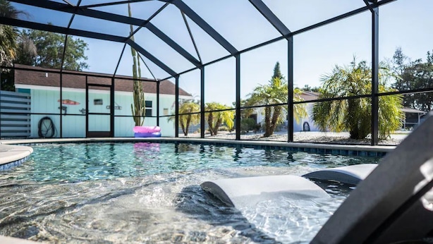A swimming pool with a hot tub area, surrounded by a glass enclosure, and palm trees in the background. - The Dolphin (Nokomis)