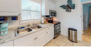 A kitchen with white cabinets, a stainless steel sink, a microwave, an oven, and a trash can. - The Dolphin (Nokomis)