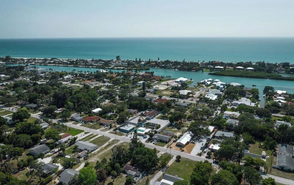 An aerial view of a coastal residential area with houses, roads, and a marina.