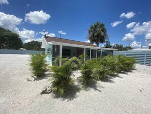 A small, single-story building with a sloped roof, surrounded by a sandy area with palm trees. - The Dolphin (Nokomis)