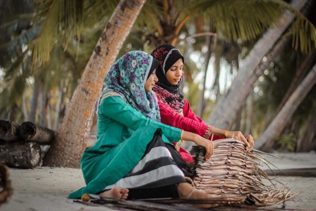 Two individuals seated outdoors, engaged in a craft activity with natural materials.