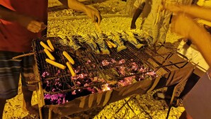 Una parrilla con salchichas y verduras asándose al aire libre.