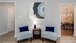 Una stanza con due poltrone decorate, un tavolino con una lampada e un grande quadro astratto appeso al muro.
