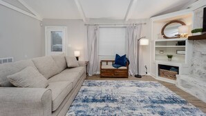 Un soggiorno con un divano color beige, un tappeto blu, una panca in legno e un camino bianco con mensole.