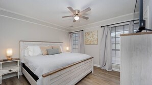 Una camera da letto con un letto in legno, una ventola a soffitto, un comodino con una lampada e una finestra con tende.