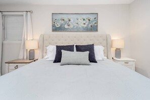 A neatly arranged bedroom with a large bed, two bedside tables, and a painting above the bed.