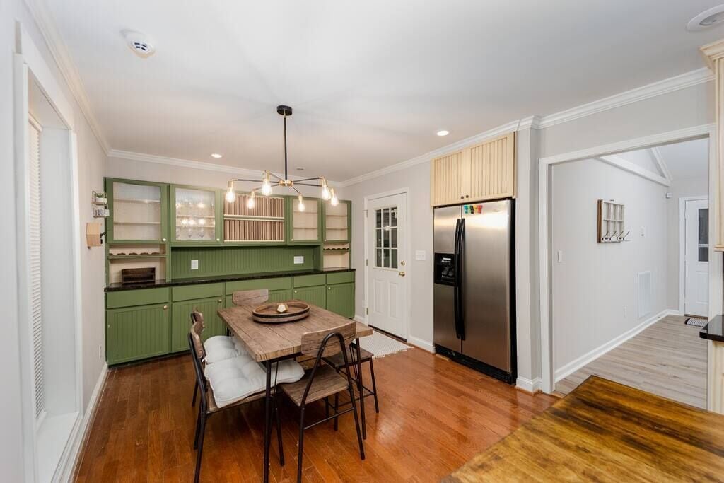 A modern kitchen with green cabinets, a wooden dining table, and a stainless steel refrigerator.