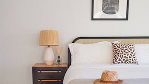 Une chambre à coucher bien rangée, avec un lit, une table de chevet, une lampe, un chapeau et un tableau encadré accroché au mur.