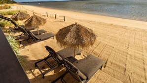 Une plage avec des chaises longues et des parasols en chaume.