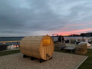 A wooden barrel structure with outdoor seating and a view of the sunset over a body of water.
