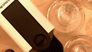Eine Nespresso-Kaffeemaschine mit Zubehör, darunter ein Pod-Halter, ein Auffangbehälter und ein Löffel.