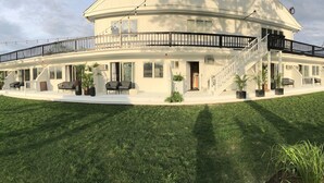 Ein großes, weißes, zweistöckiges Gebäude mit einem gebogenen Balkon, Blumentöpfen und Außenbestuhlung.