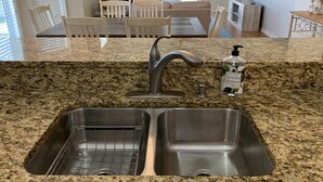 A kitchen with granite countertops, stainless steel sink, and a dining area with white chairs and a couch. - The Salty Snook in Suwannee, FL BEST LOCATION in Complex with Private Boat Slip! (Suwannee)