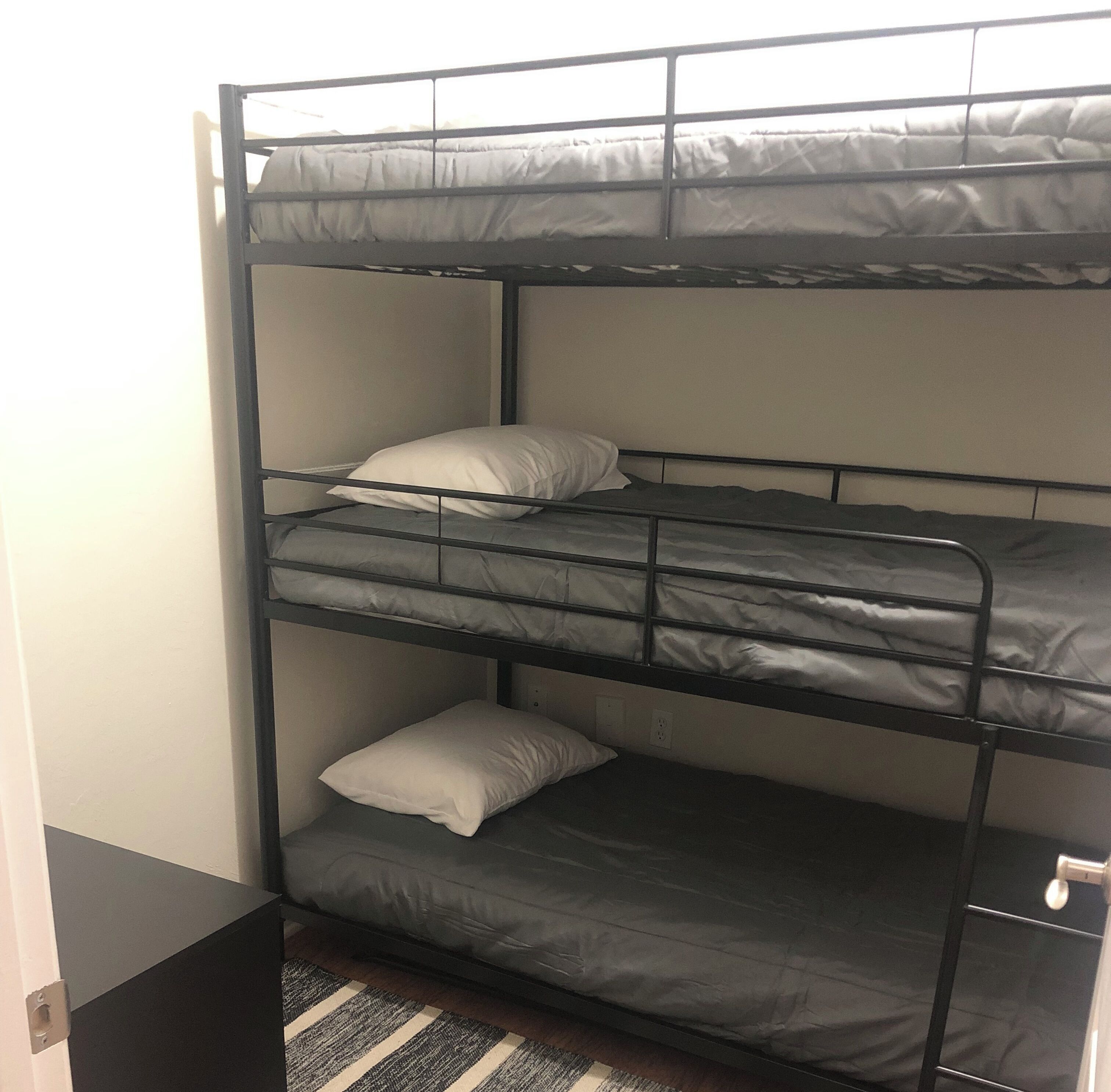A bunk bed with three levels, each with a pillow and a mattress.