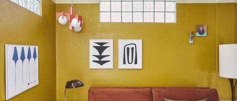 Une pièce avec un mur jaune, un canapé rouge et des œuvres d’art accrochées au mur.