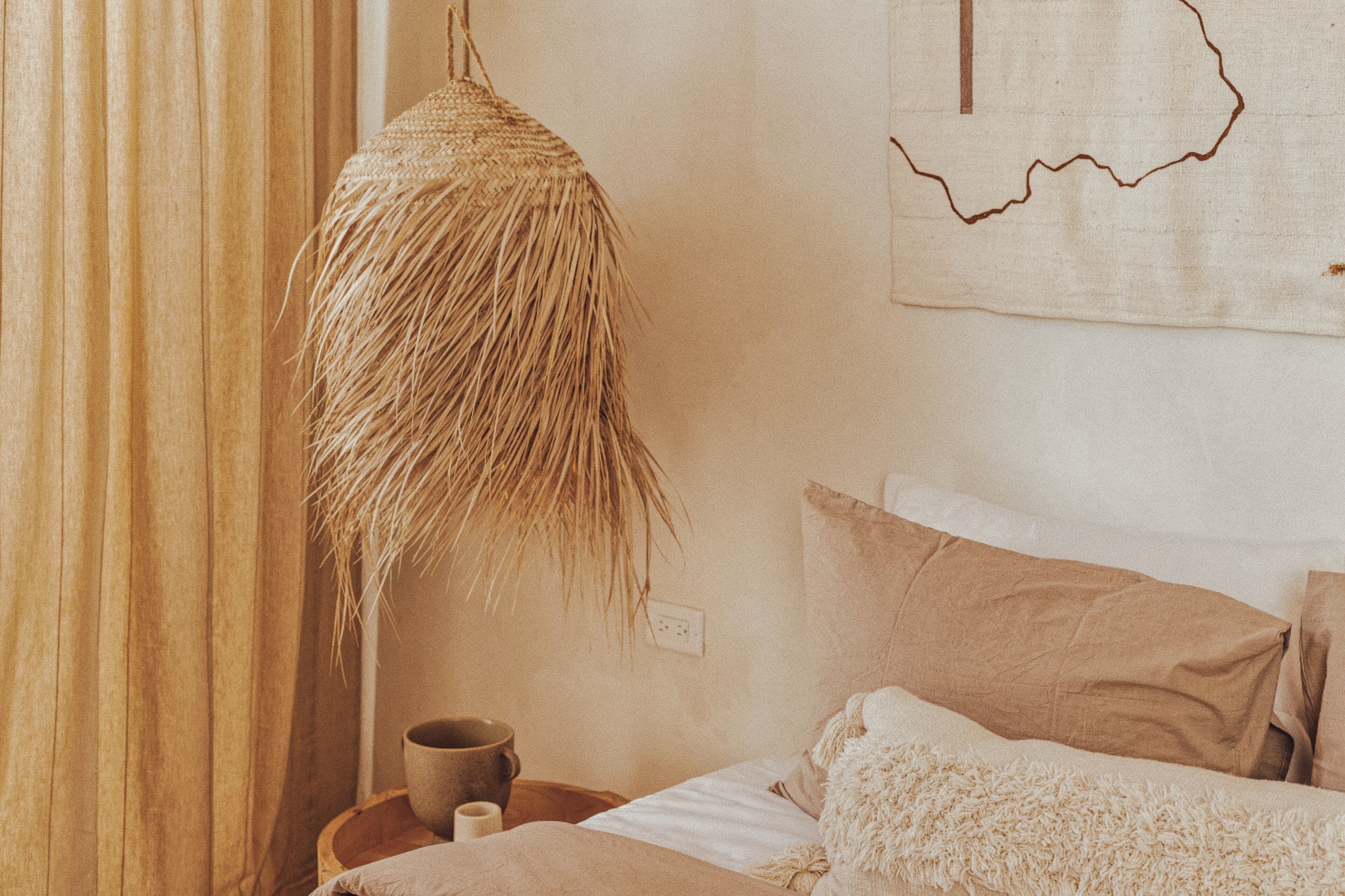 Un dormitorio con una cama, una lámpara colgante de fibra natural, un mapa en la pared y una mesita de noche de madera con una taza.