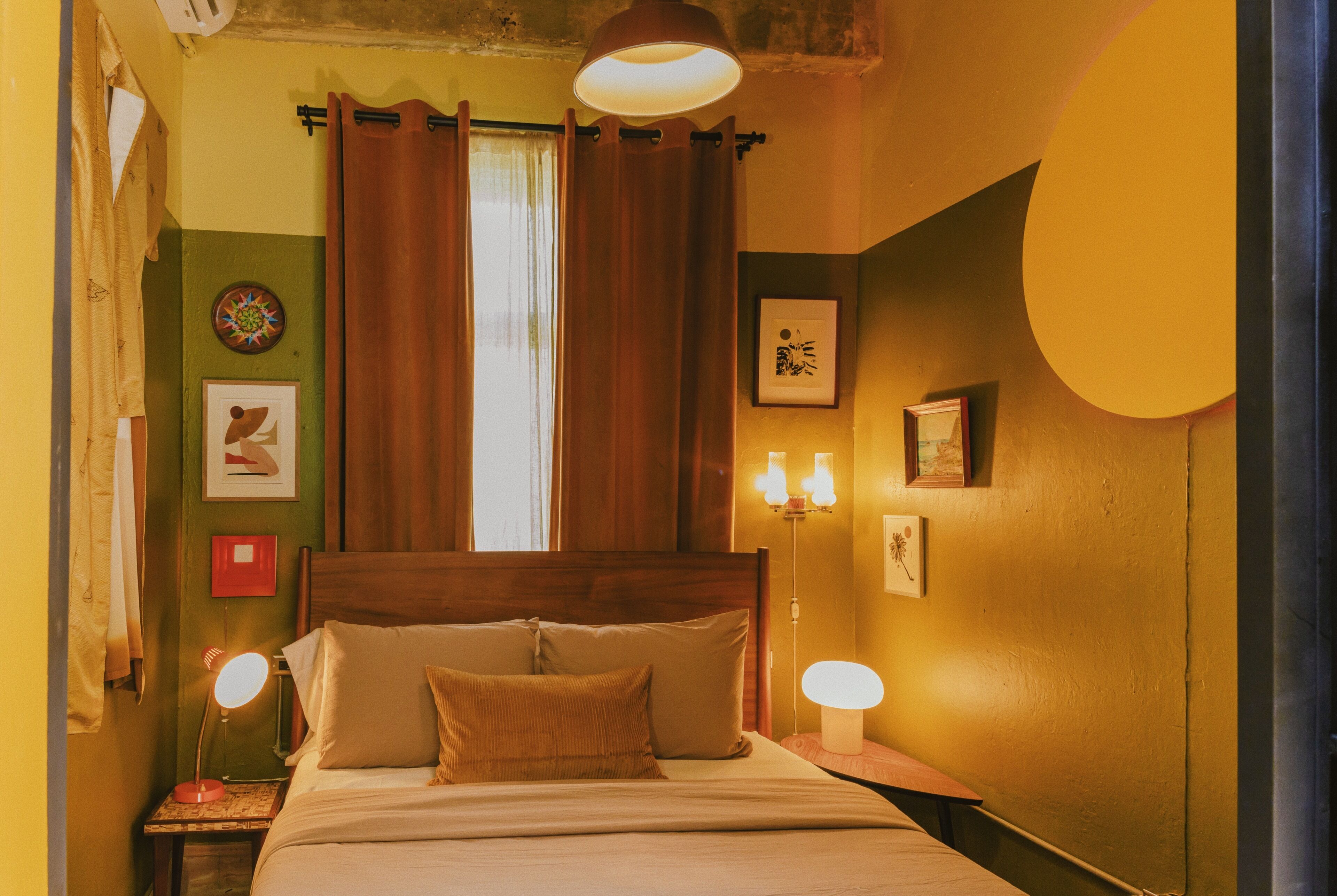 A room with a bed, two bedside lamps, a window with curtains, and wall decorations.