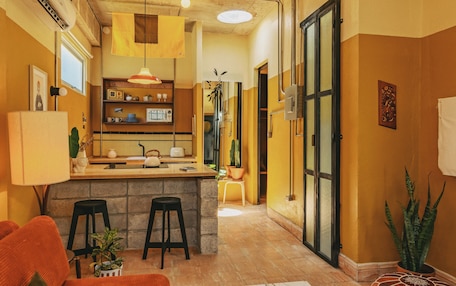 A compact kitchen with a central island, bar stools, and a hanging light fixture.